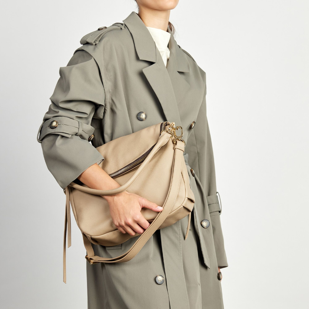 A women in a white shirt and cream pants has a black Saben Handbag across her body. The Saben handbag features a gold chain and gold saben lettering embossed at the top