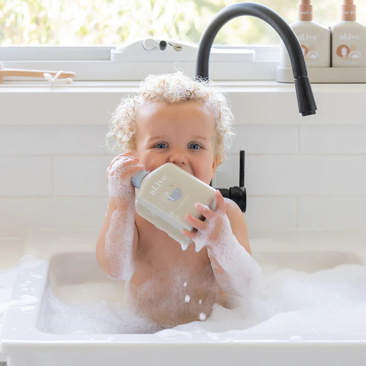Child playing with a soap dispenser in a sink filled with bubbles