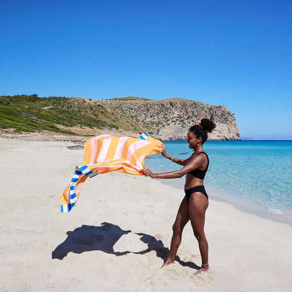 Woman on a beach holding a striped towel with a scenic background
