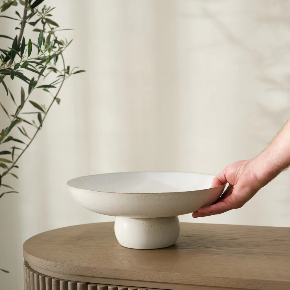 Hand holding a white ceramic dish on a wooden surface with a neutral background