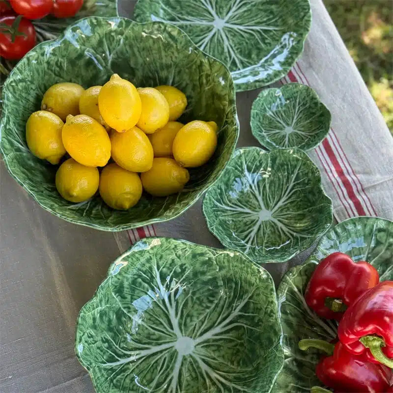Green melamine bowl with yellow fruits on a table with decorative plates and vegetables.