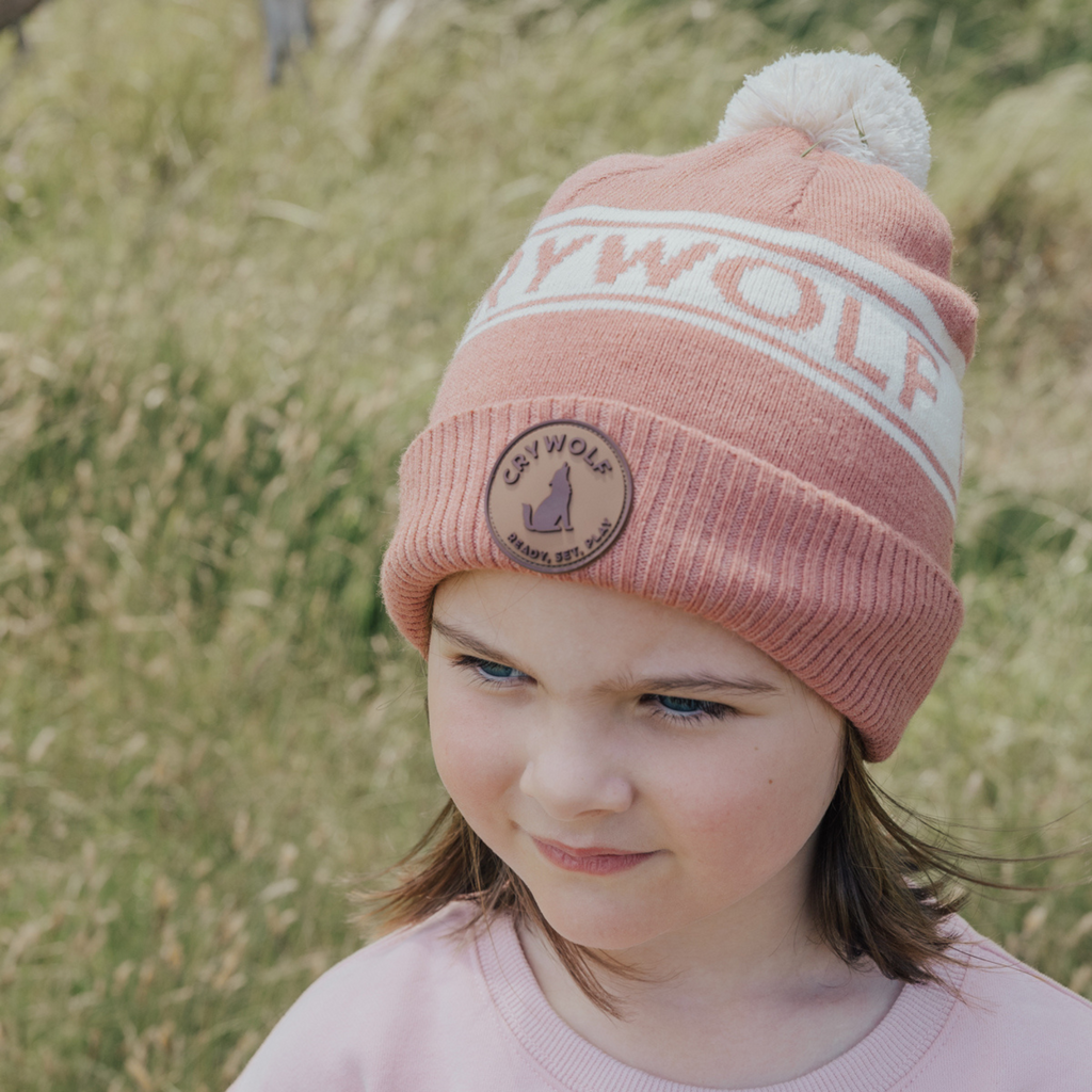 Girl wearing pink beanie with white detailing and white pompom in a field