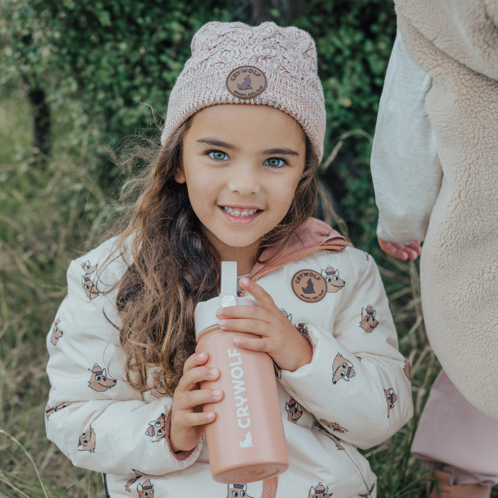 Girl outside holding a light orange colour sippy water-bottle with the text "crywolf" in white text with a wolf outline and a white coloured lid