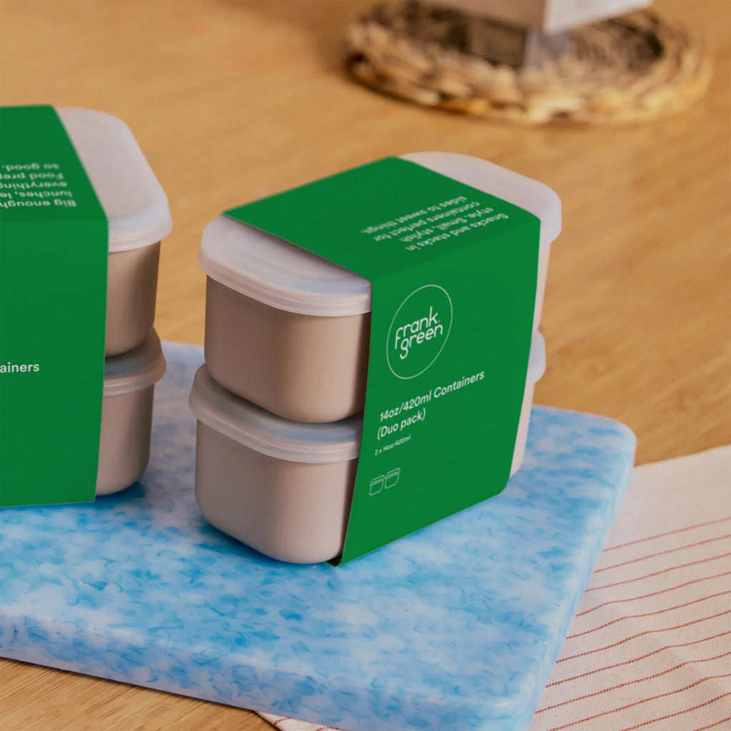 Two sets of Frank Green food containers with green packaging on a blue mat.
