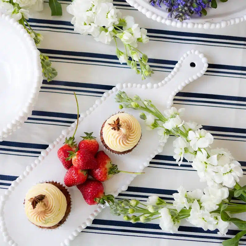Cupcakes with vanilla frosting and strawberries on a white plate with a striped tablecloth and flowers.