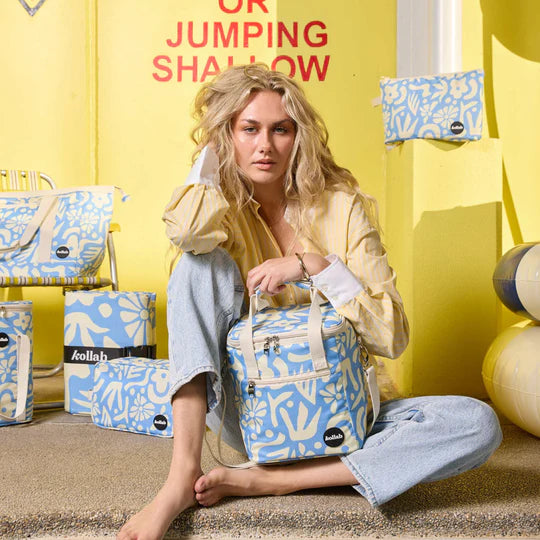 Woman holding a blue and white patterned bag against a yellow background with similar bags displayed.