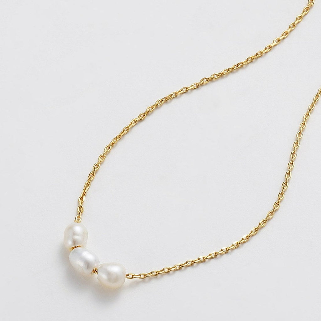 Gold necklace with three pearls on a light gray background
