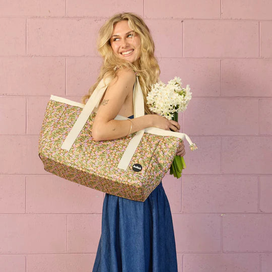 Woman holding a floral-patterned bag and flowers against a pink tiled wall