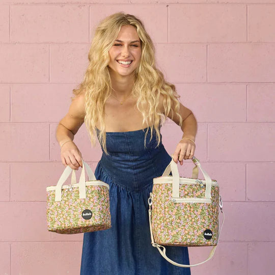 Woman holding two floral-patterned bags against a pink tiled wall