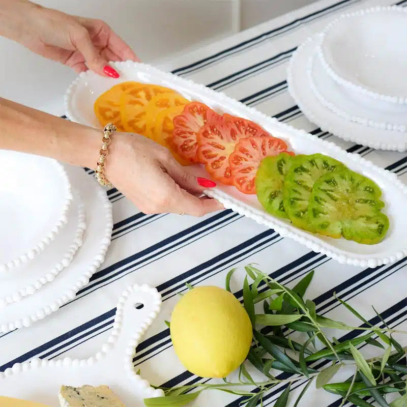 Person holding a tray of sliced tomatoes on a striped tablecloth with a lemon and herbs.