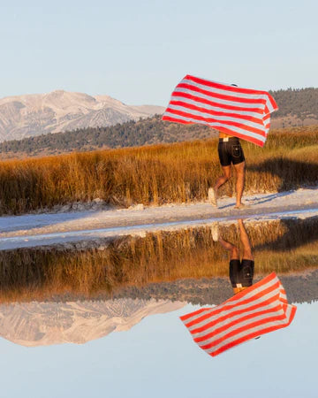 Person holding a red and white striped towel in a natural setting with mountains and water.