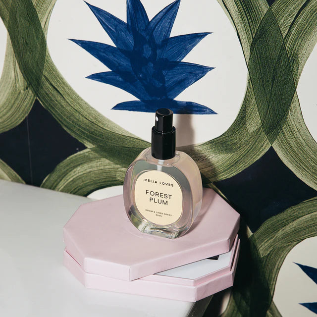 Perfume bottle labeled 'Forest Plum' on a pink stand with decorative background