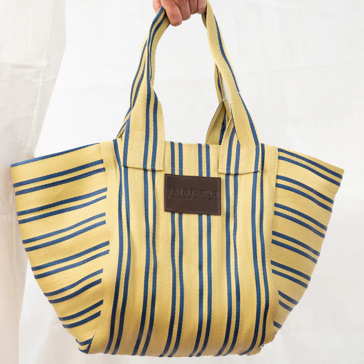 Yellow and blue striped tote bag held by a person on a white background