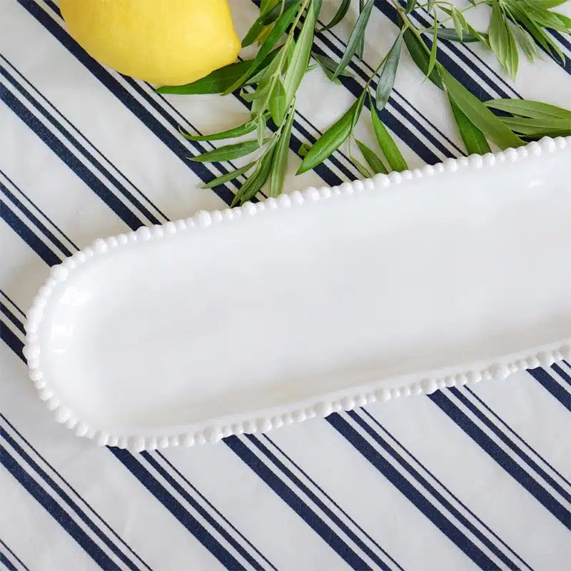 White decorative tray on a blue and white striped surface with a lemon and greenery.