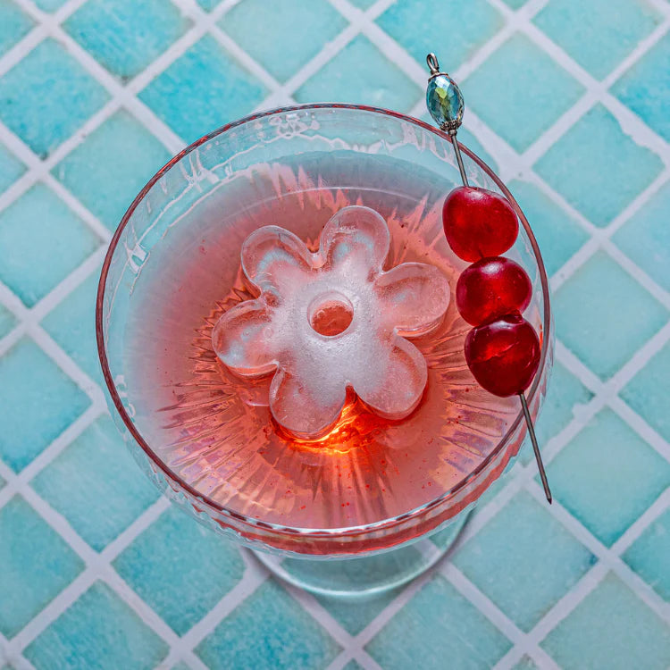 Cocktail with a flower-shaped ice cube and red berries on a turquoise tiled background