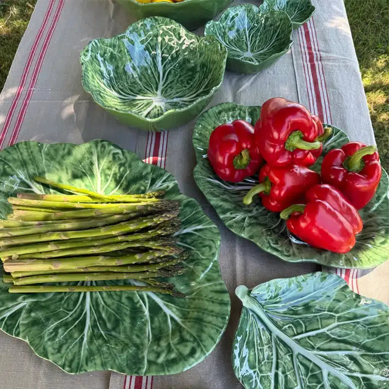 Green ceramic plates shaped like vegetables with asparagus, red peppers, and cabbage leaves on a tablecloth.