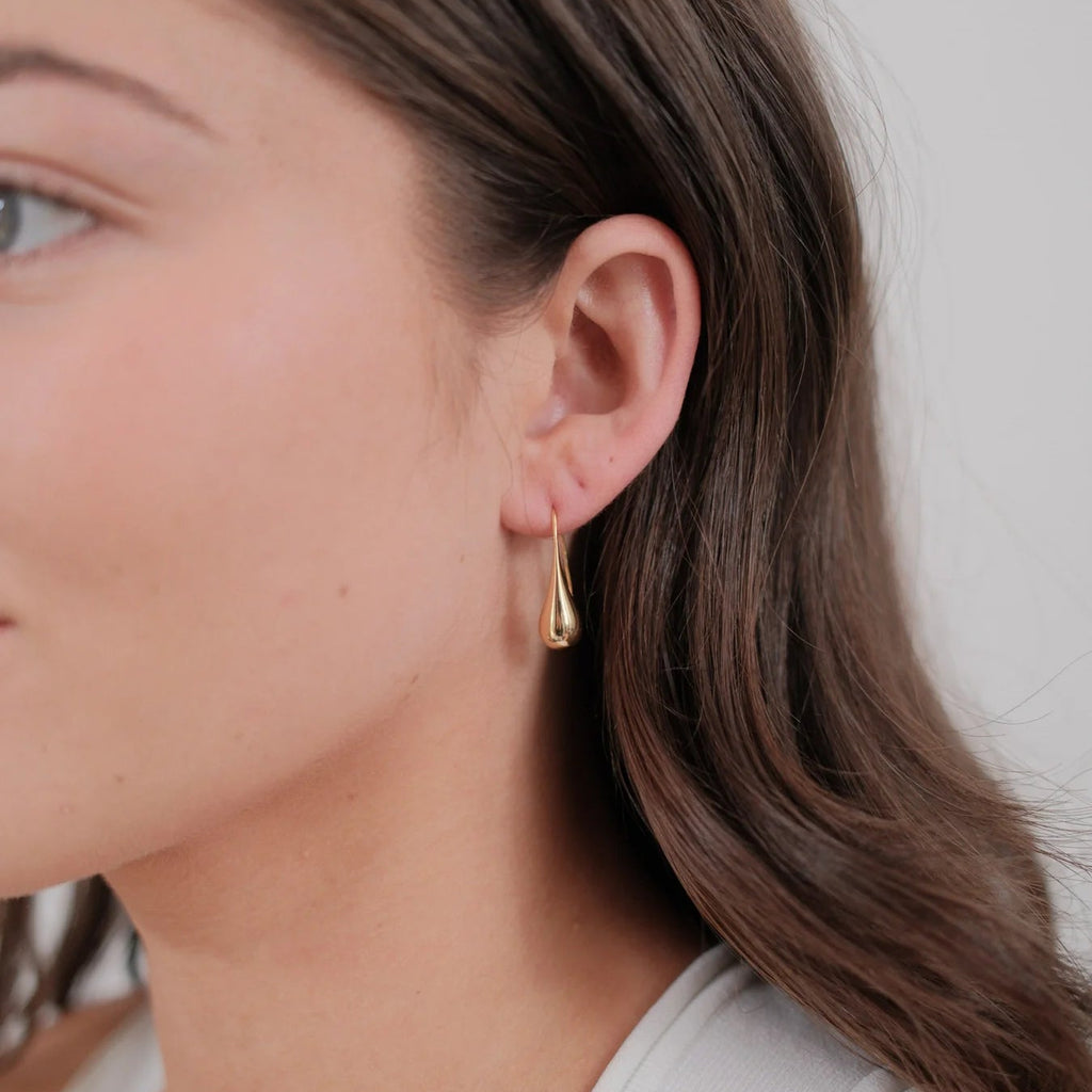 Close-up of a woman wearing gold earrings with a neutral background