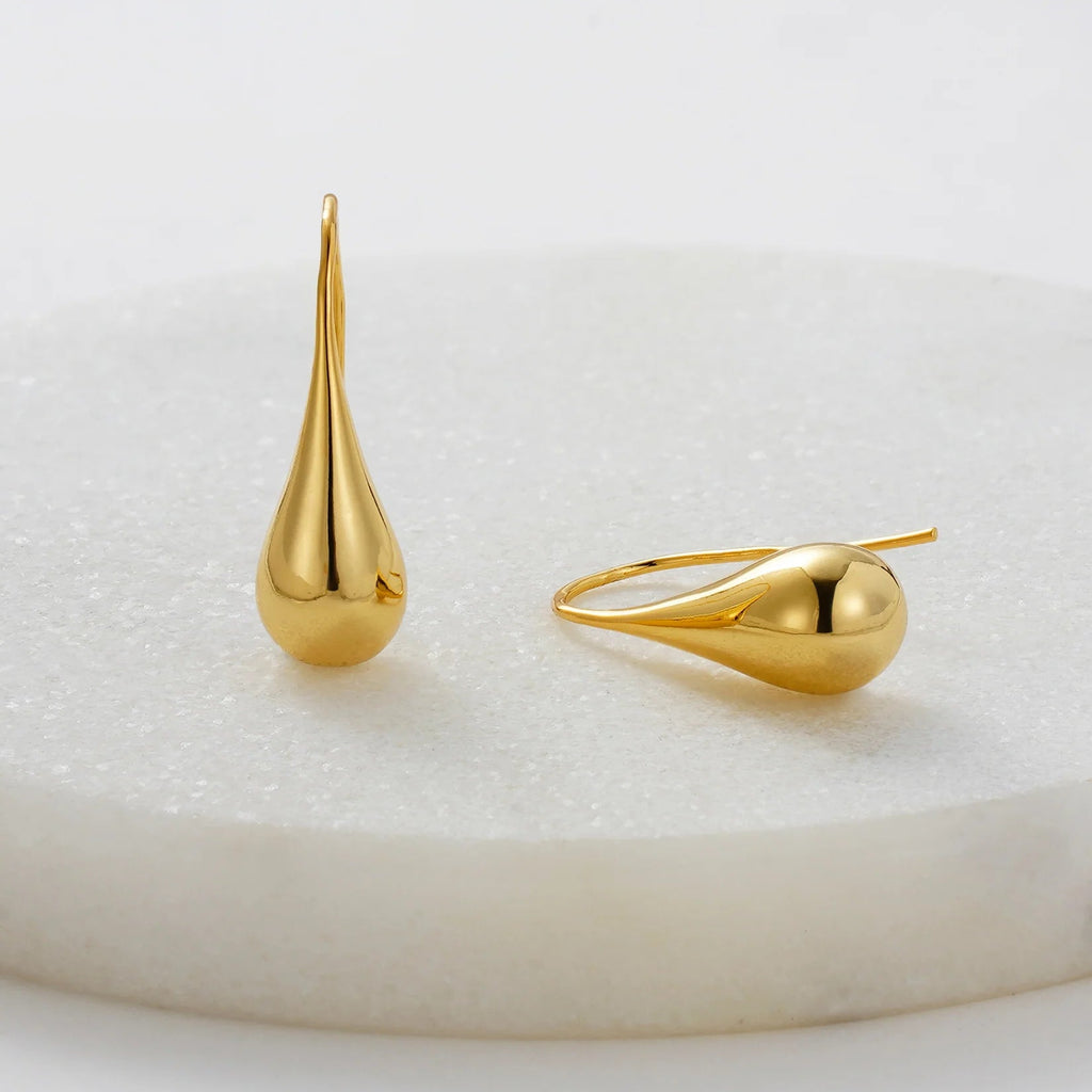 Gold teardrop-shaped earrings on a white surface