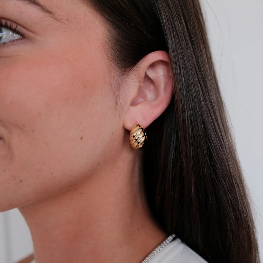 Close-up of a woman wearing gold hoop earrings with a neutral background