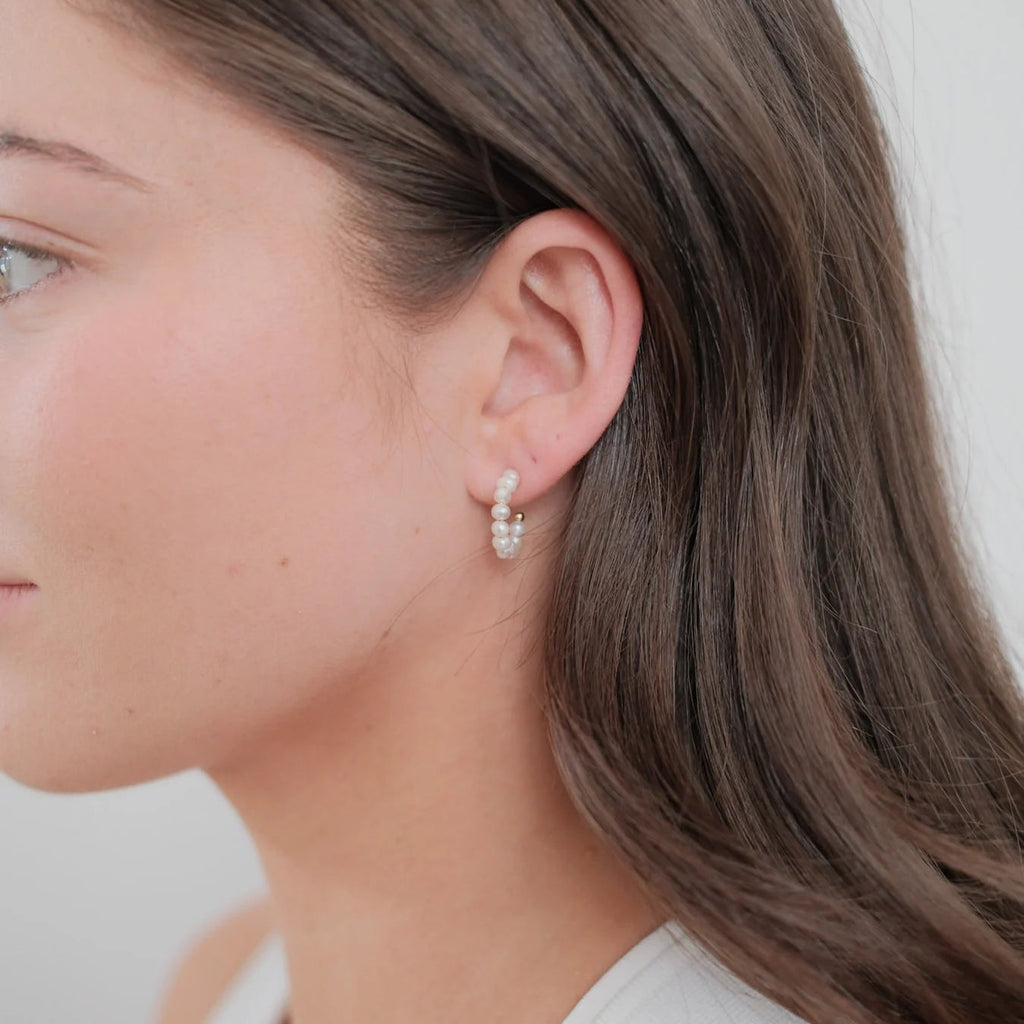 Close-up of a woman wearing pearl earrings with a plain background