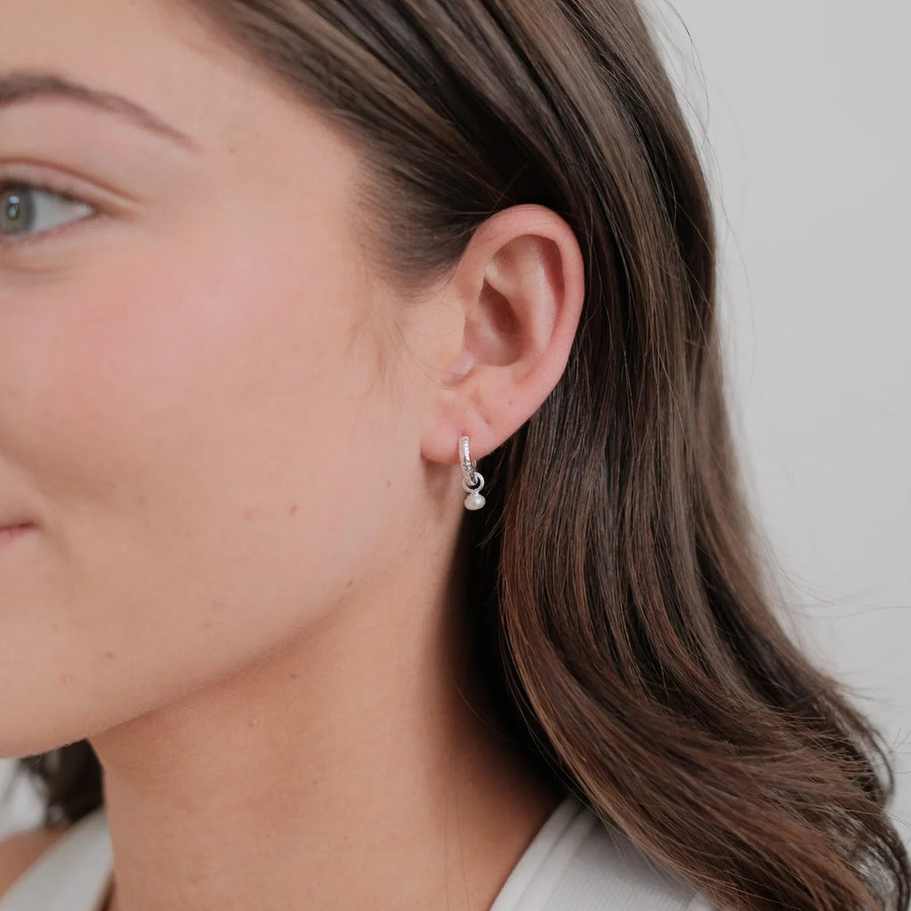 Close-up of a woman wearing pearl earrings against a neutral background