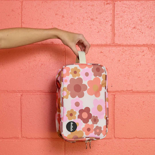 Floral-patterned pouch held by a hand against a pink brick wall