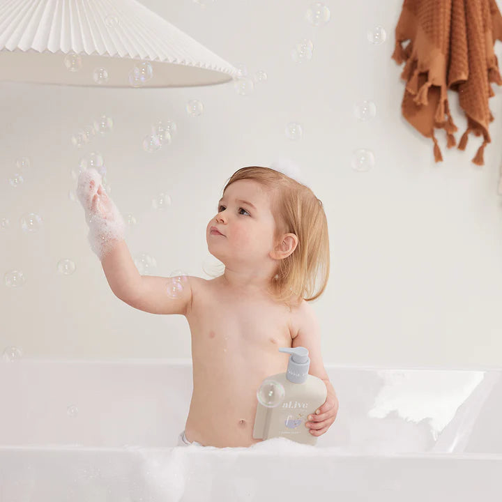 Child in a bathtub with bubbles, holding a bottle of shampoo or conditioner.