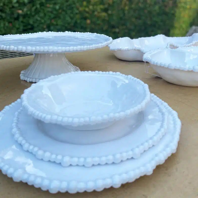 Set of white melamine dishes with textured rim on a wooden surface