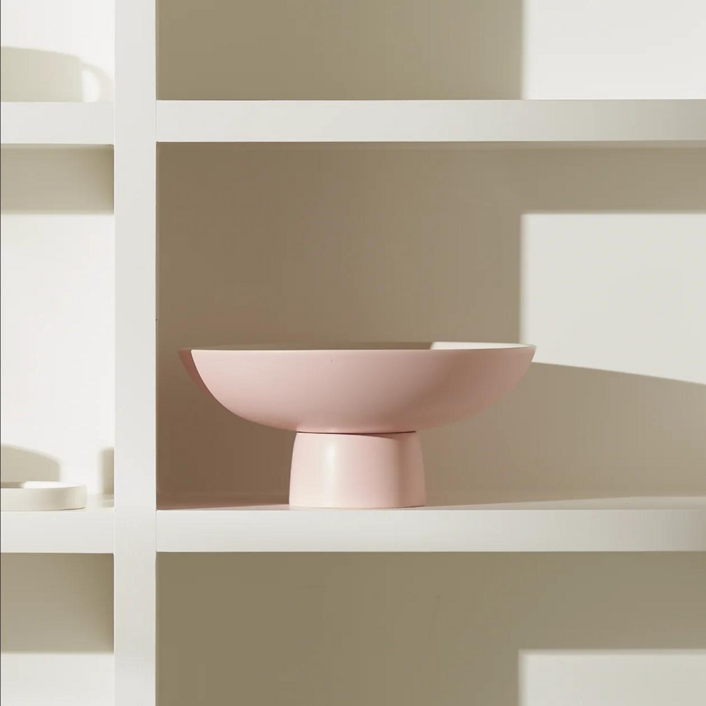 A pink pedestal bowl  on a white empty wall shelving unit 