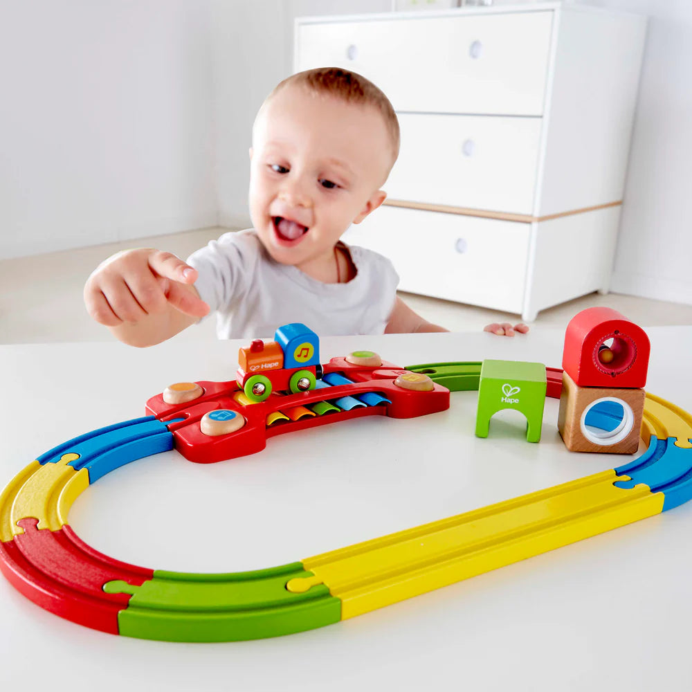 Child playing with a colorful toy train set on a white surface