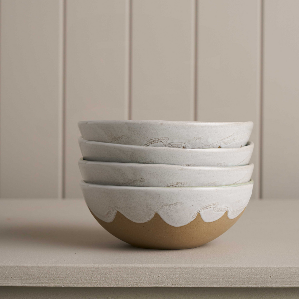 A set of four brown ceramic bowl with a white glaze inner and top with a scalloped edge against a grey boarded background 