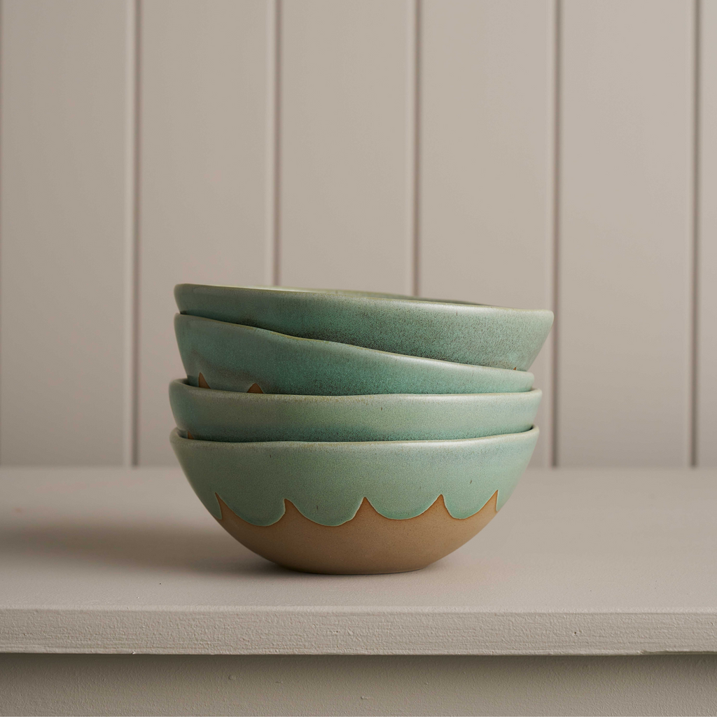 A stack of 4 ceramic green glazed bowls displayed on a grey shelf against a grey panelled wall 