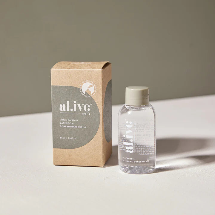 Clear bottle with cap of bathroom cleaning concentrate  and cardboard box labeled 'al.ive' on a light surface.