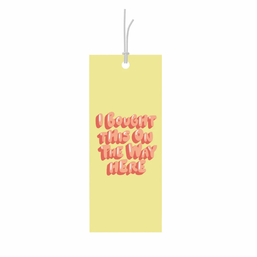 Yellow gift tag reading "I bought this on the way here" in orange text