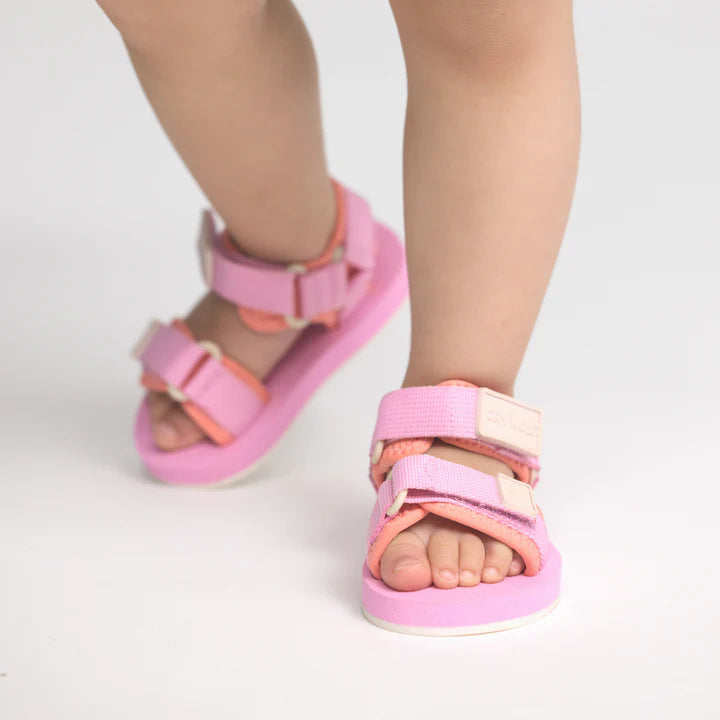 Pink and orange sandals worn by a child on a light gray background