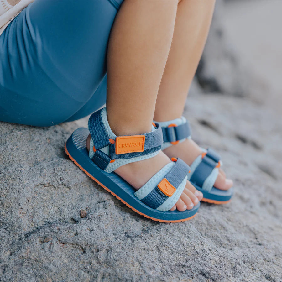 Child wearing blue sandals with orange accents on a sandy surface