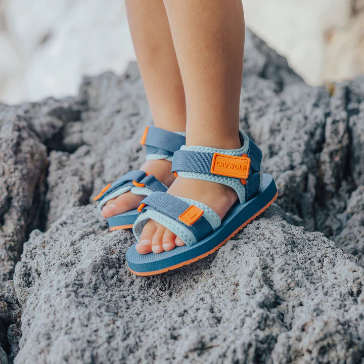 Children's blue sandals with orange accents on a rocky surface