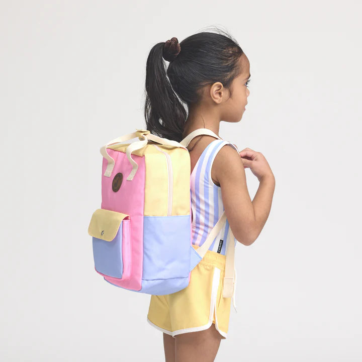 Girl wearing a colorful patchwork backpack on a plain background