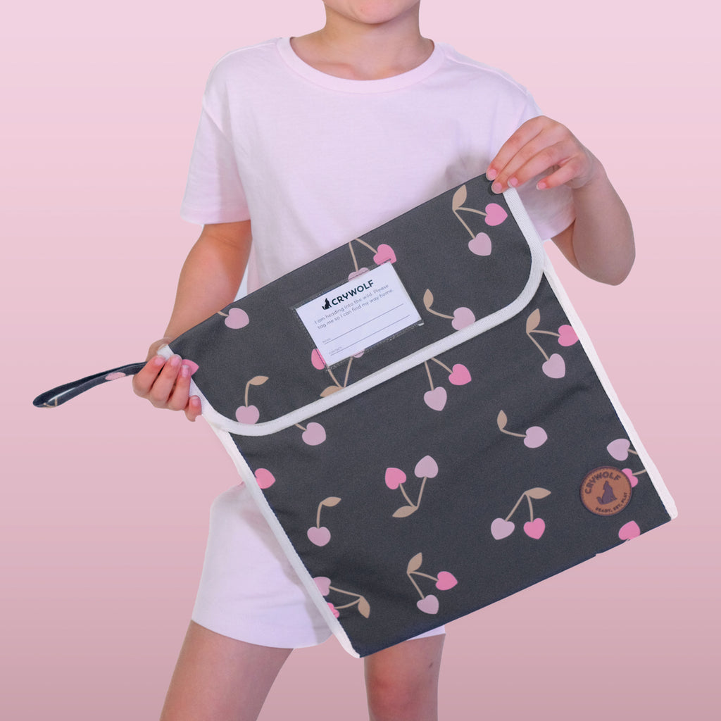 Person holding a black pouch with pink cherry pattern against a pink background