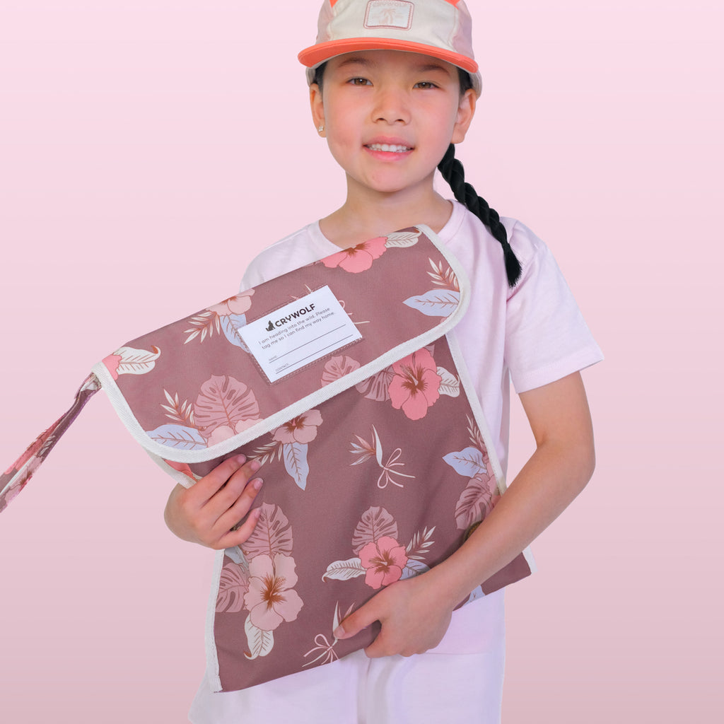 Child holding a floral-patterned umbrella with a visible brand label against a pink background