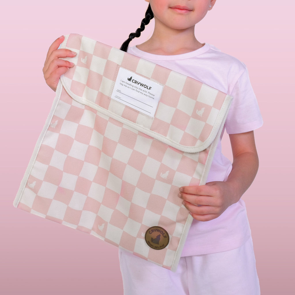 Child holding a pink and white checkered bag with a visible brand label against a pink background