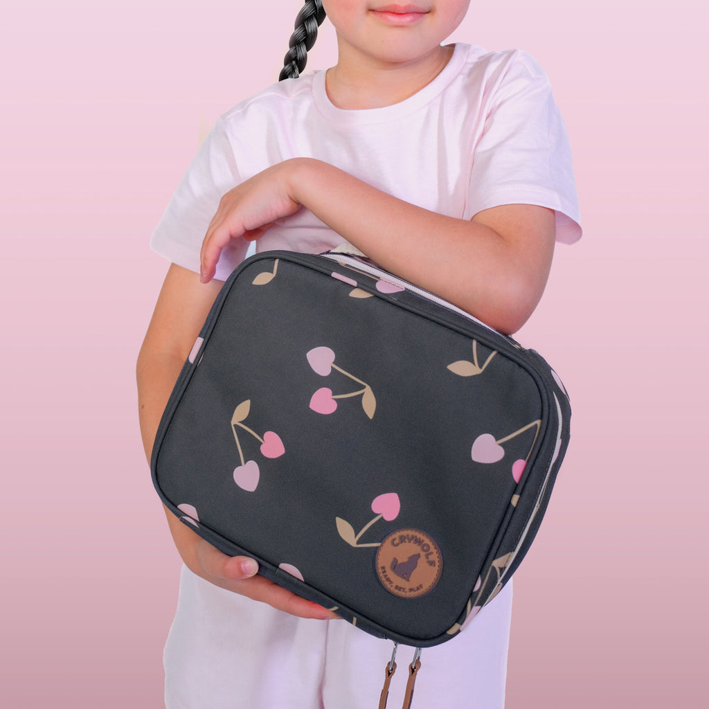 Child holding a dark gray toiletry bag with cherry pattern on a pink background
