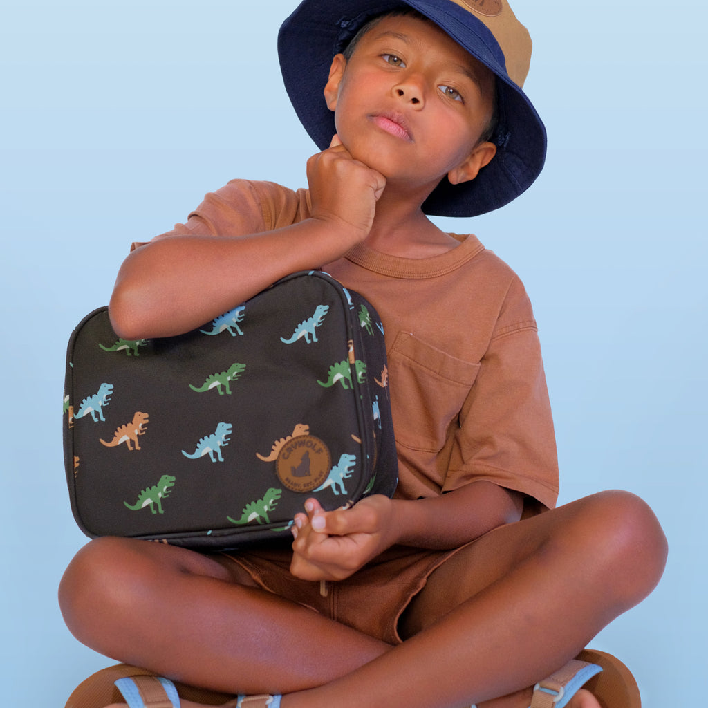 Child holding a dinosaur-patterned suitcase against a light blue background