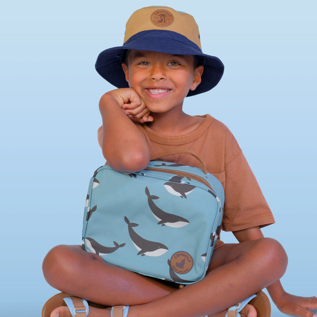 Child wearing a blue bucket hat and holding a blue bag with whale patterns against a light blue background
