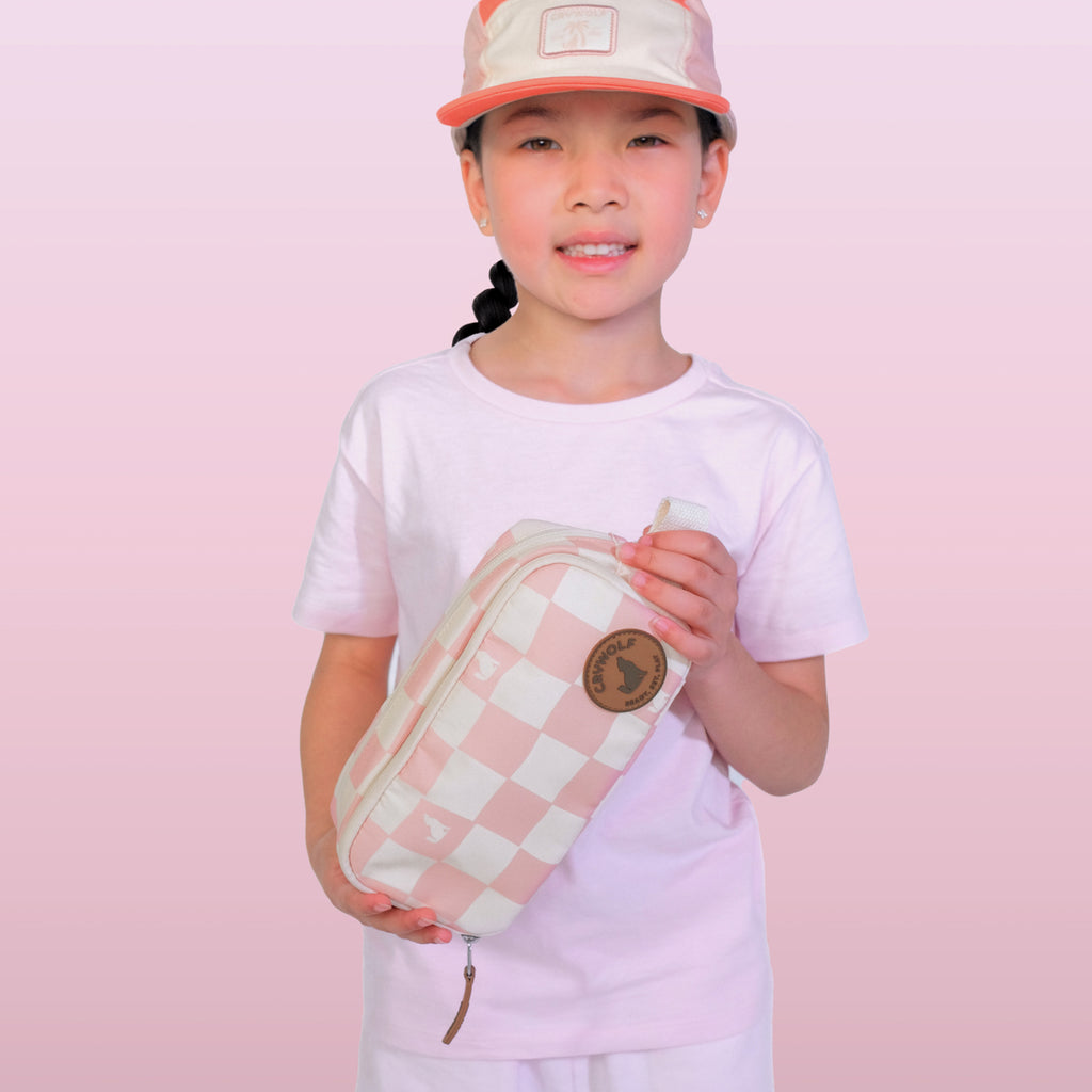 Child holding a pink checkered pouch against a pink background