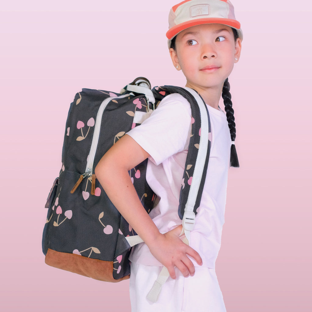 Child with a dark backpack featuring cherry designs on a pink background