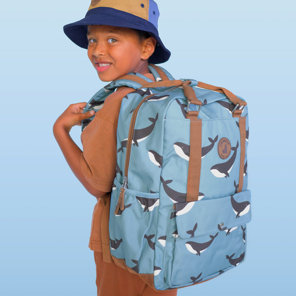 Child wearing a blue backpack with whale pattern against a light blue background