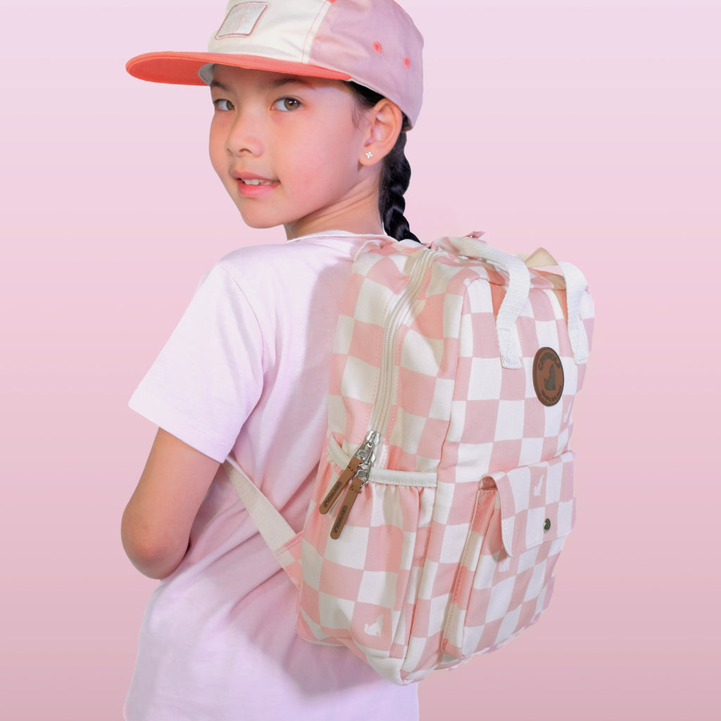 Child wearing a pink and white checkered backpack against a pink background