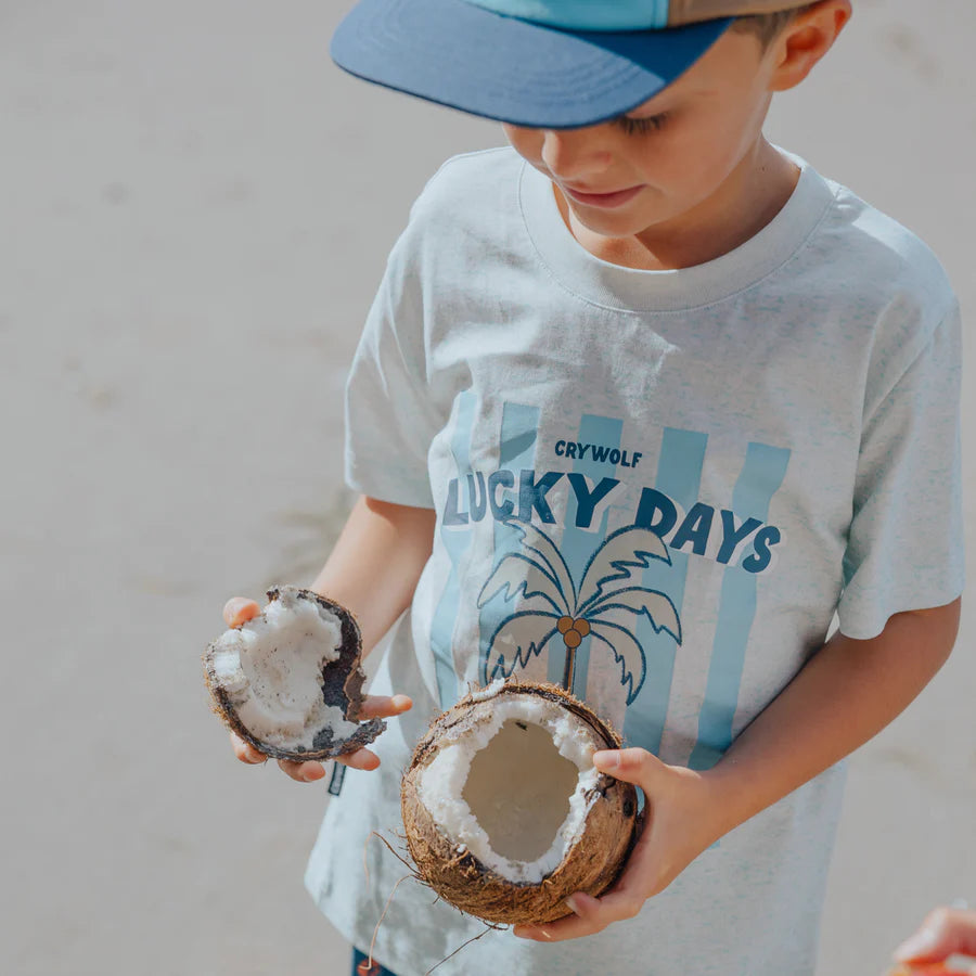 Child wearing a 'Lucky Days' t-shirt holding two coconuts.