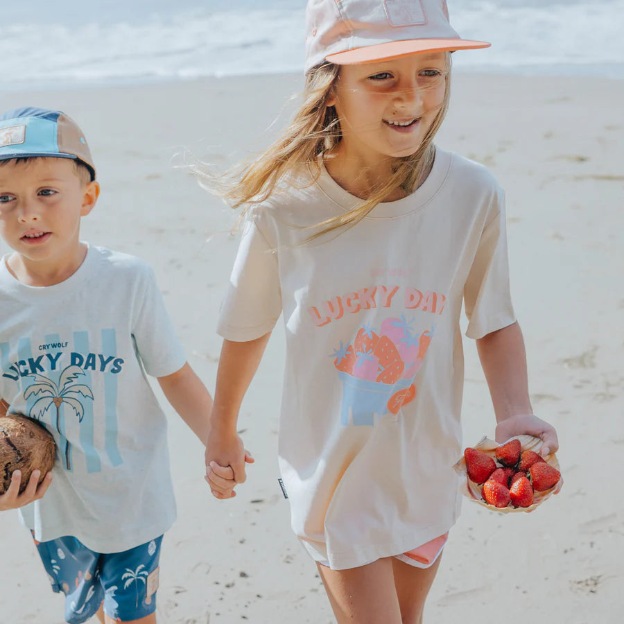 Two children on a beach holding hands, wearing 'Lucky Days' t-shirts.